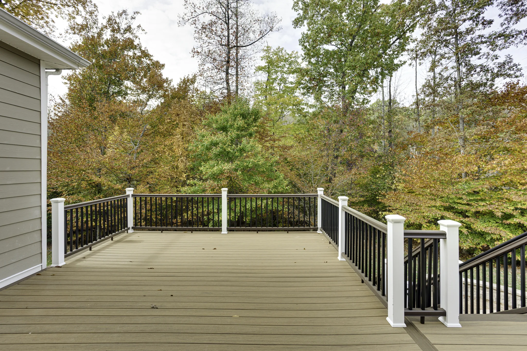 Raised deck with black metal railings and a stair run descending into a sloped wooded yard