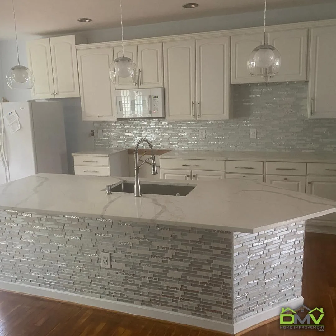 Kitchen with white shaker cabinets, a quartz island and a glass mosaic tile backsplash